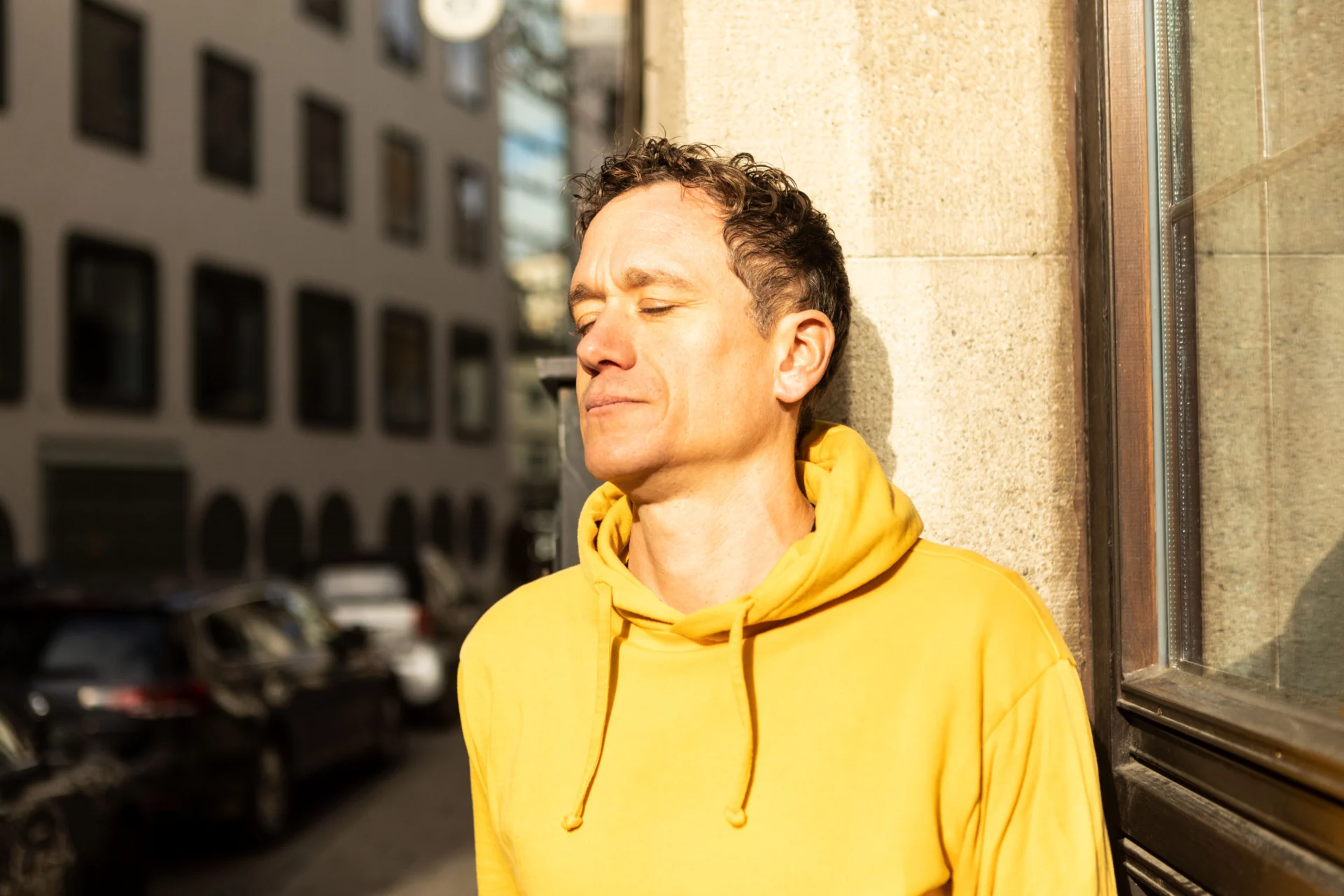 Mirco lehnt mit geschlossenen Augen an einer Wand - die Sonne strahlt ihm ins Gesicht