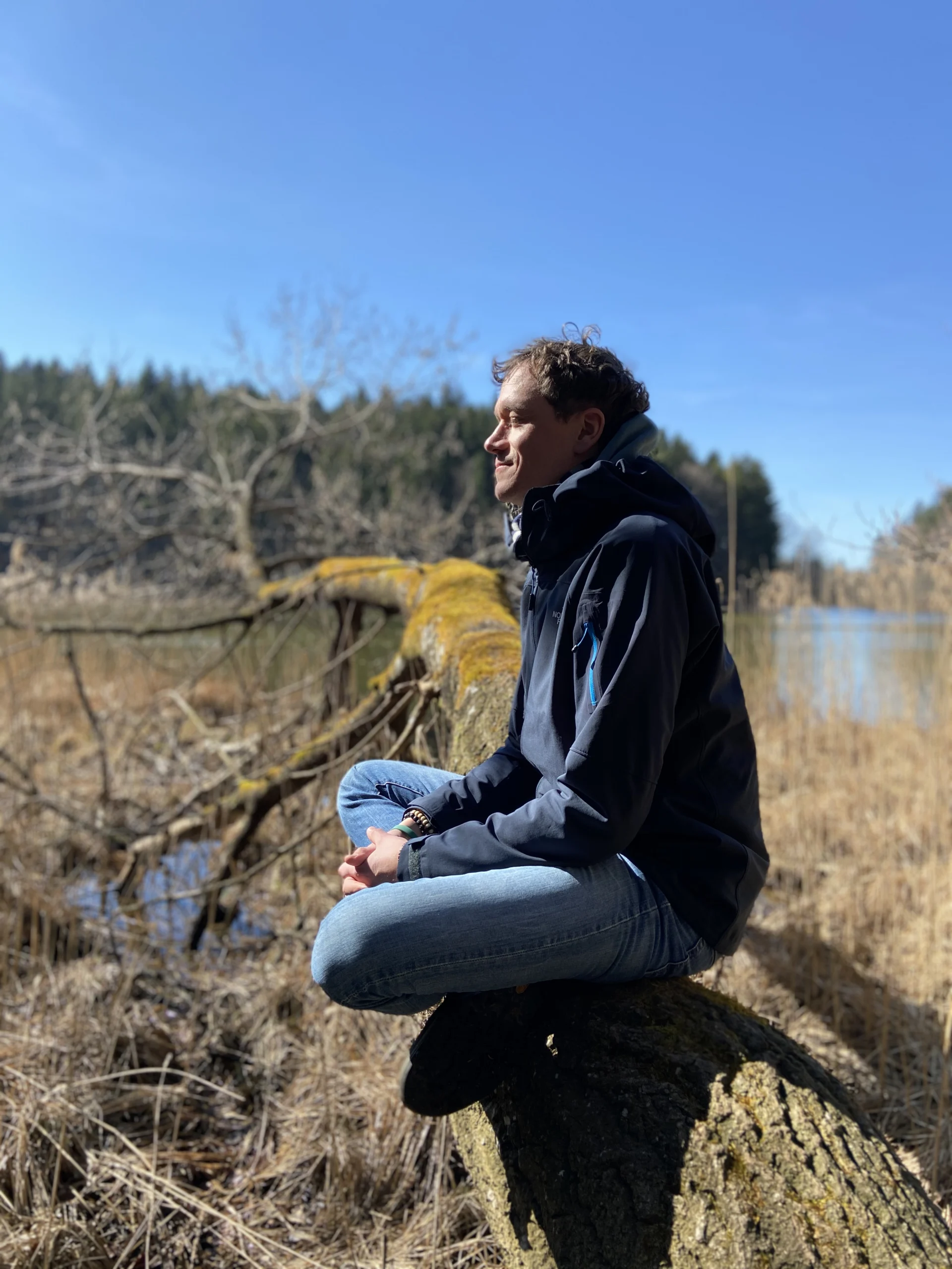 Mirco meditiert auf Baumstamm am See.